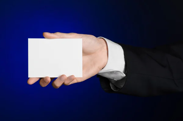 Business and advertising topic: Man in black suit holding a white blank card in his hand on a dark blue background in studio isolated — Stock Photo, Image