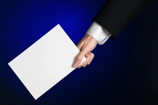 Business en reclame onderwerp: Man in zwart pak met een witte Blanco kaart in zijn hand op een donker blauwe achtergrond in studio geïsoleerd — Stockfoto