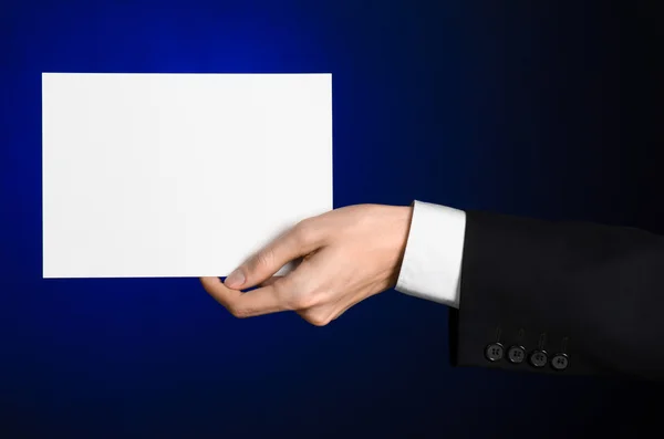 Business en reclame onderwerp: Man in zwart pak met een witte Blanco kaart in zijn hand op een donker blauwe achtergrond in studio geïsoleerd — Stockfoto