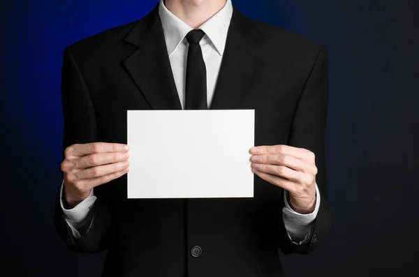 Argomento commerciale e pubblicitario: Uomo in abito nero con una carta bianca in mano su uno sfondo blu scuro in studio isolato — Foto Stock