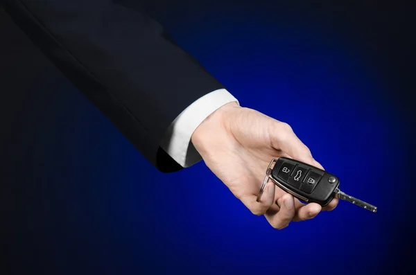 Business- en schenkingsrechten thema: autoverkoper in een zwart pak omvat de sleutels naar een nieuwe auto op een donker blauwe achtergrond in studio — Stockfoto