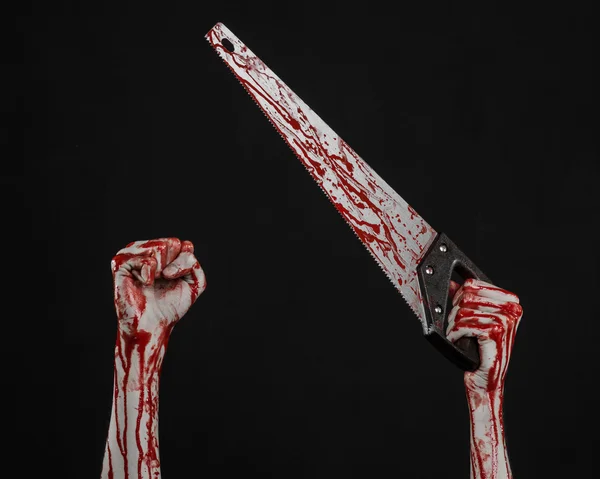 Halloween theme: bloody hand holding a bloody saw on a black background — Stock Photo, Image
