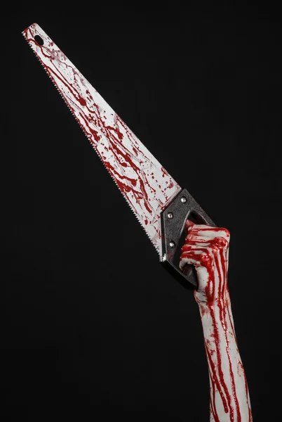 Halloween theme: bloody hand holding a bloody saw on a black background — Stock Photo, Image