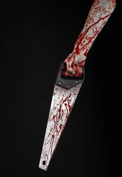 Halloween theme: bloody hand holding a bloody saw on a black background — Stock Photo, Image