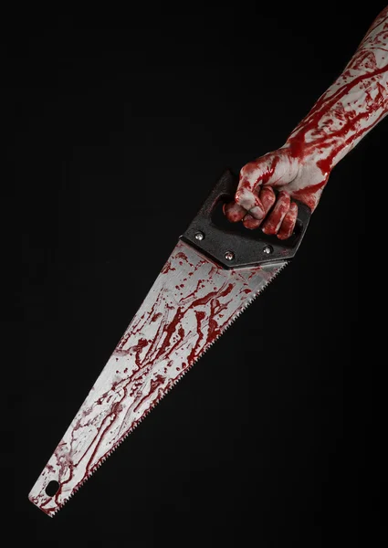 Halloween theme: bloody hand holding a bloody saw on a black background — Stock Photo, Image