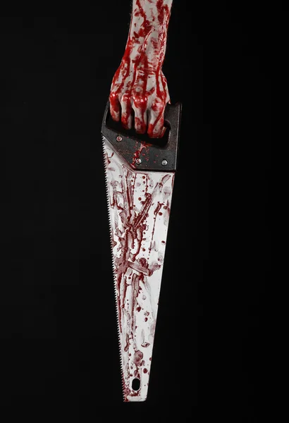 Halloween theme: bloody hand holding a bloody saw on a black background — Stock Photo, Image