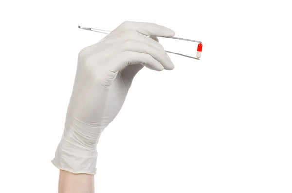 Фармакологія та медична тема: рука лікаря в білій рукавичці тримає пінцет з червоною капсулою ізольовано на білому тлі в студії — стокове фото