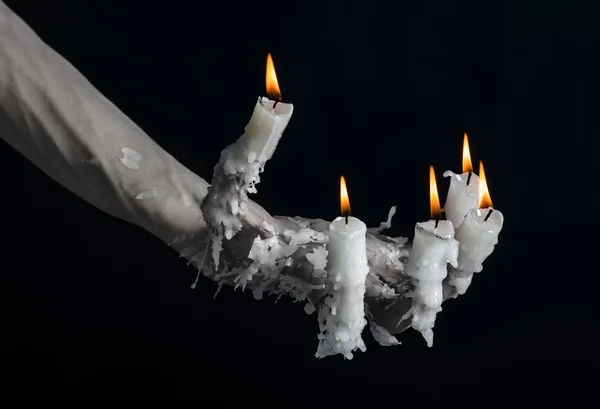 Halloween theme: on the hand wearing a candle and dripping melted wax on black isolated background