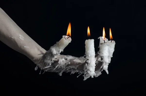 Halloween theme: on the hand wearing a candle and dripping melted wax on black isolated background