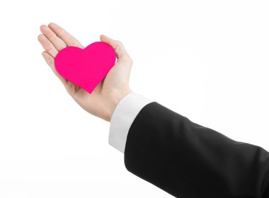 Sevgililer günü ve aşk şarkısı: Studio beyaz bir arka plan üzerinde izole bir pembe kalp tutan siyah elbiseli bir adam