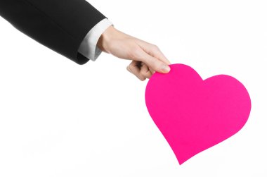 Sevgililer günü ve aşk şarkısı: Studio beyaz bir arka plan üzerinde izole bir pembe kalp tutan siyah elbiseli bir adam