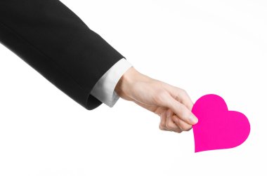 Sevgililer günü ve aşk şarkısı: Studio beyaz bir arka plan üzerinde izole bir pembe kalp tutan siyah elbiseli bir adam