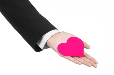 Sevgililer günü ve aşk şarkısı: Studio beyaz bir arka plan üzerinde izole bir pembe kalp tutan siyah elbiseli bir adam