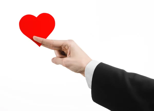 Tema del Día de San Valentín y el amor: un hombre con un traje negro sosteniendo un corazón rojo aislado sobre un fondo blanco en el estudio — Foto de Stock