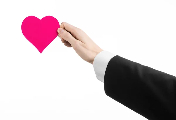 Tema del Día de San Valentín y el amor: un hombre con un traje negro sosteniendo un corazón rosa aislado sobre un fondo blanco en el estudio — Foto de Stock