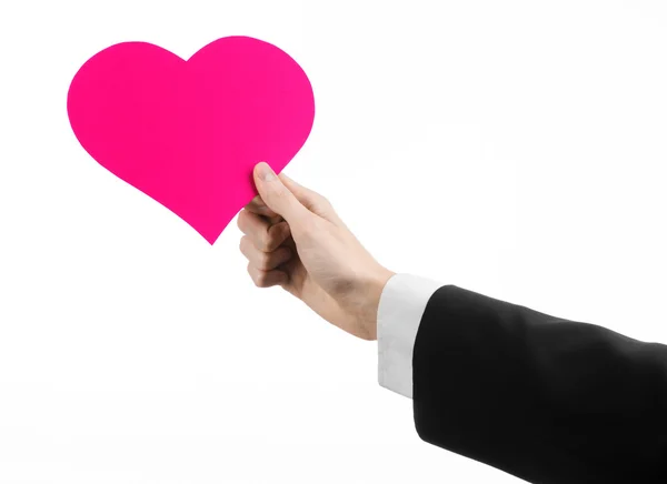 Tema del Día de San Valentín y el amor: un hombre con un traje negro sosteniendo un corazón rosa aislado sobre un fondo blanco en el estudio — Foto de Stock