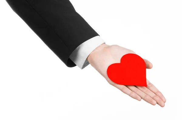 Tema del Día de San Valentín y el amor: un hombre con un traje negro sosteniendo un corazón rojo aislado sobre un fondo blanco en el estudio — Foto de Stock