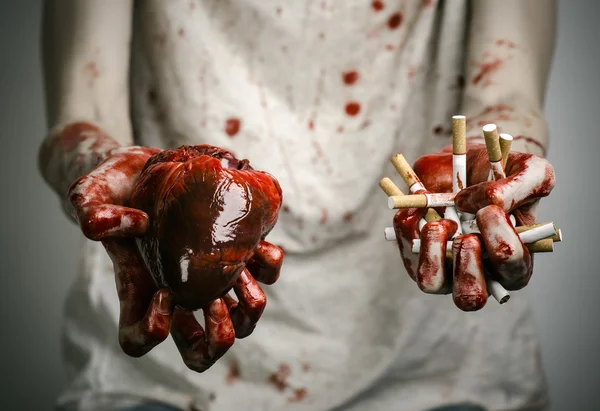 Publicidad social y control del tabaco: mano ensangrentada sosteniendo un cigarrillo fumador y corazón humano ensangrentado —  Fotos de Stock