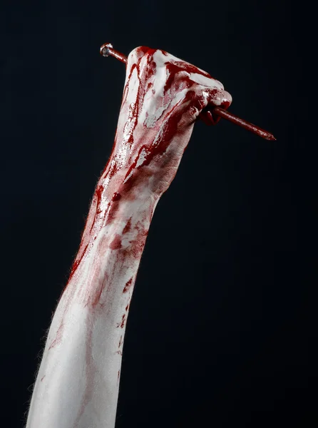 Bloody Halloween theme: bloody hand holding a large sharp nail isolated on black background in studio — Stock Photo, Image