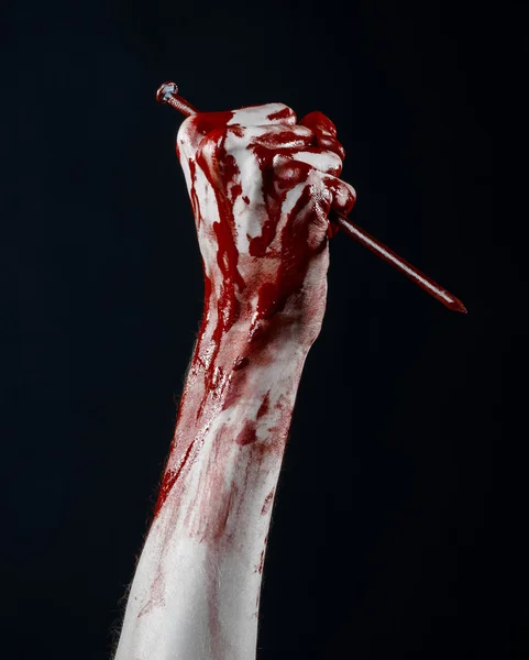 Bloody Halloween theme: bloody hand holding a large sharp nail isolated on black background in studio — Stock Photo, Image