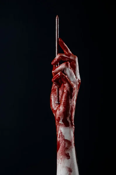 Tema sângeroasă de Halloween: mână sângeroasă care ține o unghie mare ascuțită izolată pe fundal negru în studio — Fotografie, imagine de stoc