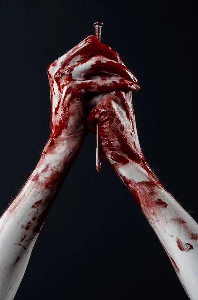 Bloody Halloween theme: bloody hand holding a large sharp nail isolated on black background in studio — Stock Photo, Image