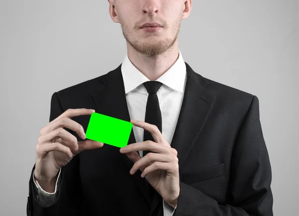 Empresário em um terno preto e gravata preta segurando um cartão, uma mão segurando um cartão, cartão verde, cartão é inserido, o cartão-chave croma verde, fundo cinza, isolado, tema de negócios, tema da banca — Fotografia de Stock