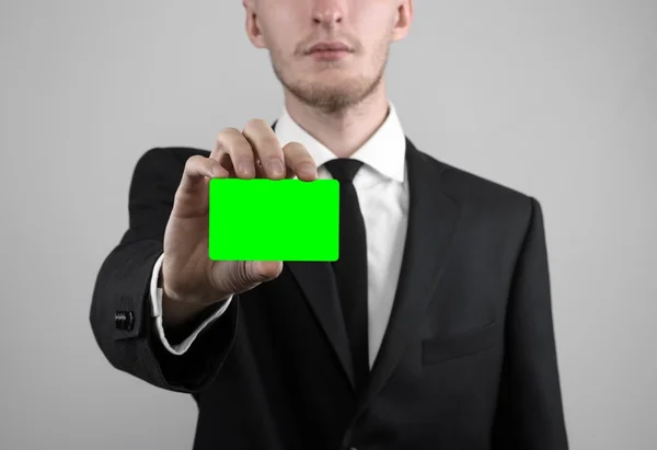 Empresário em um terno preto e gravata preta segurando um cartão, uma mão segurando um cartão, cartão verde, cartão é inserido, o cartão-chave croma verde, fundo cinza, isolado, tema de negócios, tema da banca — Fotografia de Stock