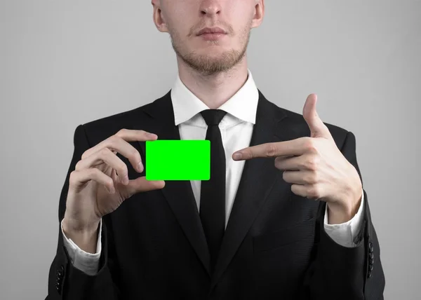 Empresário em um terno preto e gravata preta segurando um cartão, uma mão segurando um cartão, cartão verde, cartão é inserido, o cartão-chave croma verde, fundo cinza, isolado, tema de negócios, tema da banca — Fotografia de Stock