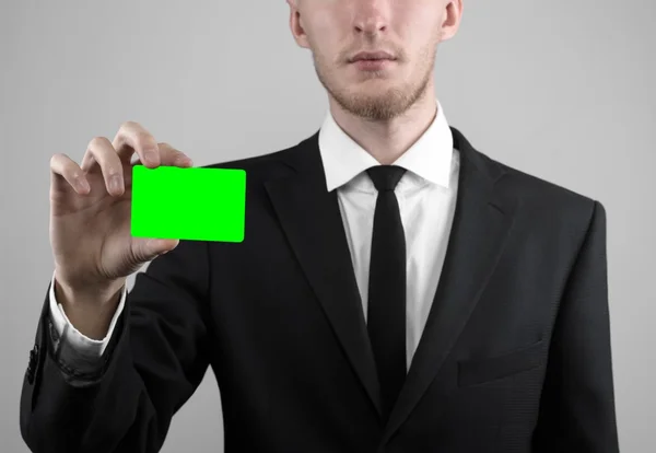 Empresário em um terno preto e gravata preta segurando um cartão, uma mão segurando um cartão, cartão verde, cartão é inserido, o cartão-chave croma verde, fundo cinza, isolado, tema de negócios, tema da banca — Fotografia de Stock