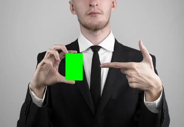 Επιχειρηματία σε ένα μαύρο κοστούμι και εκμετάλλευση μαύρη γραβάτα που τοποθετείτε μια κάρτα, ένα χέρι που κρατά μια κάρτα, πράσινο κάρτα, κάρτα, κάρτα πράσινο chroma-κλειδί, γκρι φόντο, απομονωμένες, επιχειρηματικές θέμα, θέμα των τραπεζικών — Φωτογραφία Αρχείου