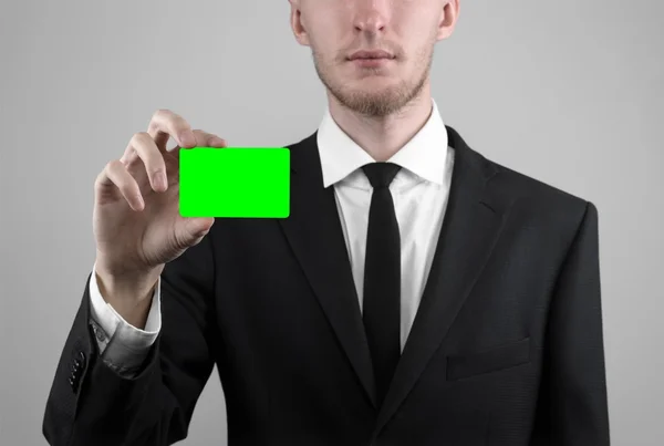 Empresário em um terno preto e gravata preta segurando um cartão, uma mão segurando um cartão, cartão verde, cartão é inserido, o cartão-chave croma verde, fundo cinza, isolado, tema de negócios, tema da banca — Fotografia de Stock