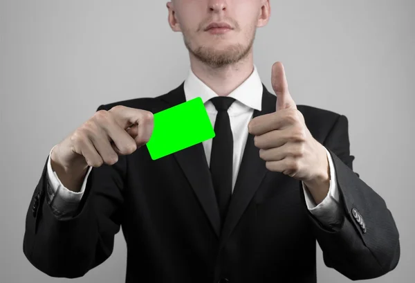 Empresário em um terno preto e gravata preta segurando um cartão, uma mão segurando um cartão, cartão verde, cartão é inserido, o cartão-chave croma verde, fundo cinza, isolado, tema de negócios, tema da banca — Fotografia de Stock