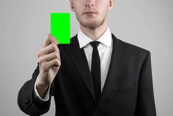 Zakenman in een zwart pak en zwarte stropdas bedrijf een kaart, een hand met een kaart, groene kaart, kaart is geplaatst, de groene chroma key-card, grijze achtergrond, geïsoleerde, zakelijke thema, thema van het bankwezen — Stockfoto