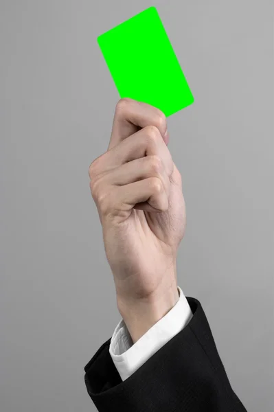 Zakenman in een zwart pak en zwarte stropdas bedrijf een kaart, een hand met een kaart, groene kaart, kaart is geplaatst, de groene chroma key-card, grijze achtergrond, geïsoleerde, zakelijke thema, thema van het bankwezen — Stockfoto
