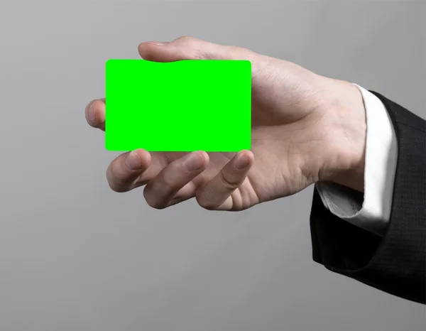 Podnikatel v černé a černou kravatu hospodářství, které je vložena karta, ruka drží kartu, Zelená karta, karta, kódovanou kartu zelené barvy, šedé pozadí, izolované, obchodní téma, téma bankovnictvi — Stock fotografie
