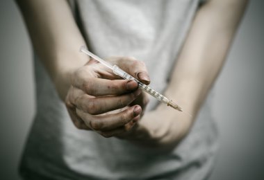 Uyuşturucu ve uyuşturucu bağımlılığı konu karşı mücadele: sıska kirli bağımlısı bir şırınga uyuşturucu ve kırmızı kalpli karanlık bir arka plan üzerinde tutan