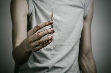Uyuşturucu ve uyuşturucu bağımlılığı konu karşı mücadele: sıska kirli bağımlısı bir şırınga uyuşturucu ve kırmızı kalpli karanlık bir arka plan üzerinde tutan
