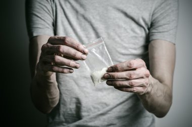 Uyuşturucu ve uyuşturucu bağımlılığı konu karşı mücadele: paket kokain gri T-shirt stüdyoda karanlık bir arka plan üzerine tutarak bağımlısı
