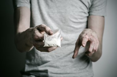 Uyuşturucu ve uyuşturucu bağımlılığı konu karşı mücadele: paket kokain gri T-shirt stüdyoda karanlık bir arka plan üzerine tutarak bağımlısı