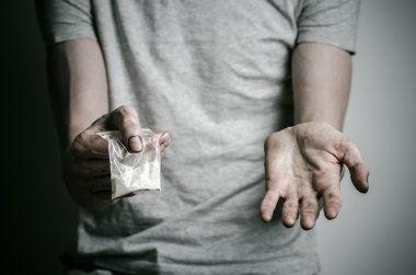 Uyuşturucu ve uyuşturucu bağımlılığı konu karşı mücadele: paket kokain gri T-shirt stüdyoda karanlık bir arka plan üzerine tutarak bağımlısı