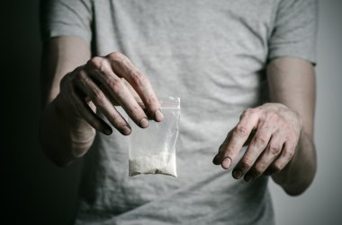 Uyuşturucu ve uyuşturucu bağımlılığı konu karşı mücadele: paket kokain gri T-shirt stüdyoda karanlık bir arka plan üzerine tutarak bağımlısı