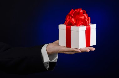Kutlamalar ve hediye Tema: Studio izole koyu mavi zemin üzerine beyaz kutu kırmızı kurdele, güzel ile sarılı özel hediye ve pahalı hediye tutarak siyah takım elbiseli bir adam