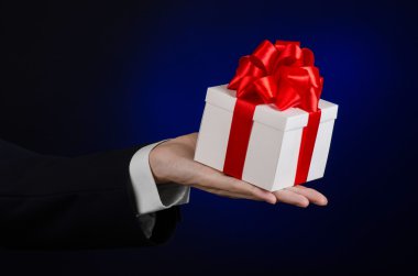 Kutlamalar ve hediye Tema: Studio izole koyu mavi zemin üzerine beyaz kutu kırmızı kurdele, güzel ile sarılı özel hediye ve pahalı hediye tutarak siyah takım elbiseli bir adam