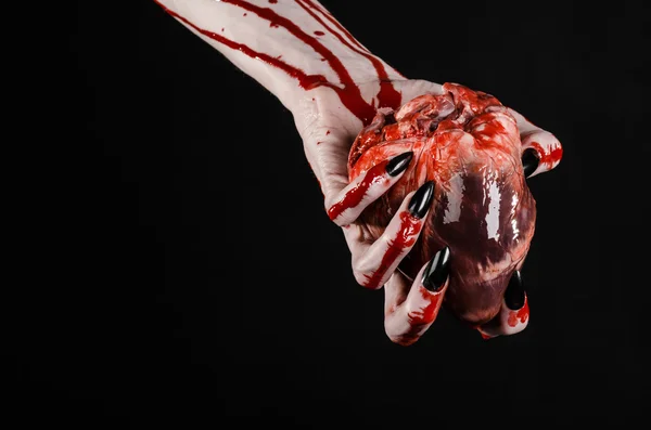 Horror sangrento e tema de Halloween: mãos sangrentas terríveis com unhas pretas segurando um coração humano sangrento em um fundo preto isolado em estúdio — Fotografia de Stock