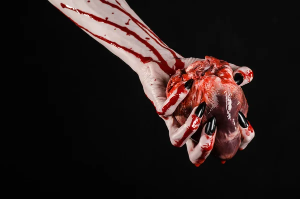 Blodig skräck och Halloween-tema: fruktansvärda blodiga händer med svarta naglar håller en blodig mänskliga hjärtat på en svart bakgrund isolerade bakgrunden i studion — Stockfoto