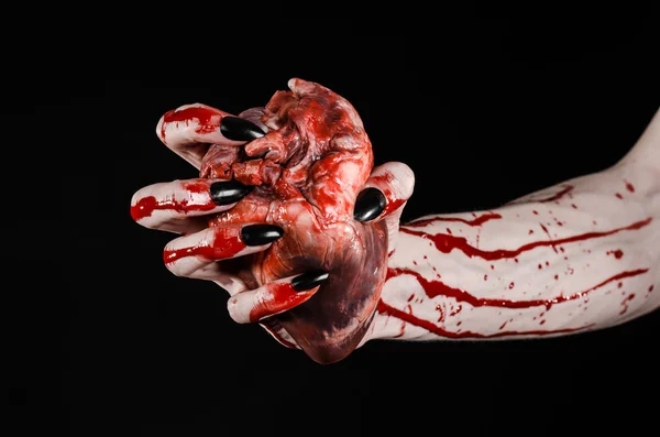 Horror sangrento e tema de Halloween: mãos sangrentas terríveis com unhas pretas segurando um coração humano sangrento em um fundo preto isolado em estúdio — Fotografia de Stock