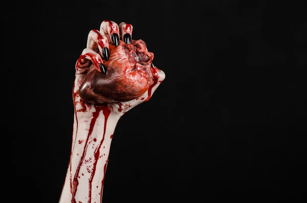 Bloedend, horror en Halloween thema: verschrikkelijk bloedige handen met zwarte nagels houden een bloedige menselijk hart op een zwarte achtergrond geïsoleerd achtergrond in studio — Stockfoto