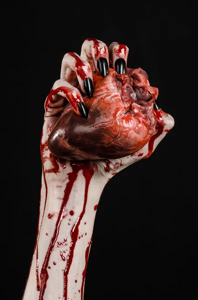Кривавий жах і тема Хеллоуїна: жахливі криваві руки з чорними цвяхами, що тримають криваве людське серце на чорному тлі ізольованому фоні в студії — стокове фото