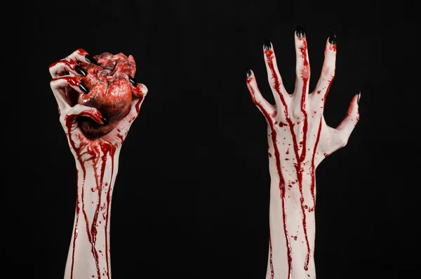 Horror sangrento e tema de Halloween: mãos sangrentas terríveis com unhas pretas segurando um coração humano sangrento em um fundo preto isolado em estúdio — Fotografia de Stock